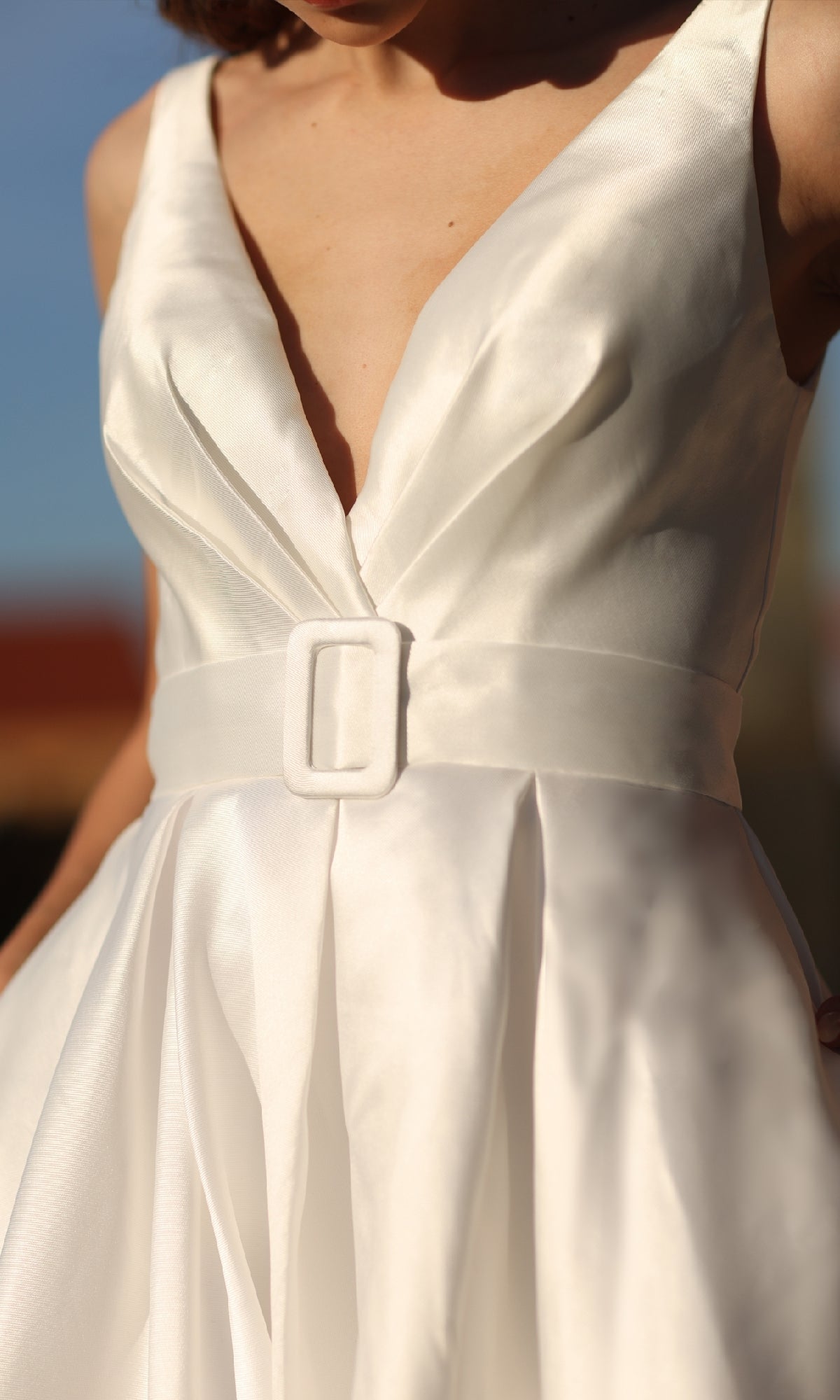 A close-up of a woman wearing the Tina Holly BB209W, a belted long white prom dress featuring a deep V-neckline and a matching rectangular-buckle belt.